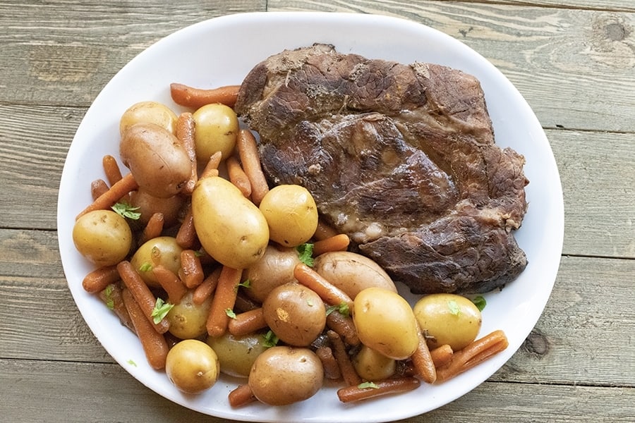 beef, potatoes and carrots on a white platter sitting on a barn board table