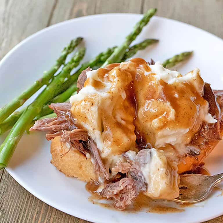 hot beef sandwich on a white plate with asparagus