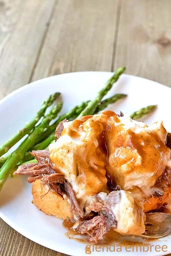 Hot beef sandwich on a white plate with asparagus.