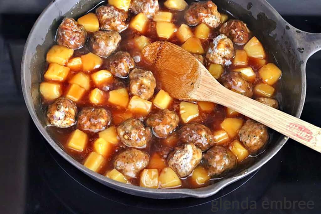 Meatballs added to the pineaplle and sauce in a cast iron skillet