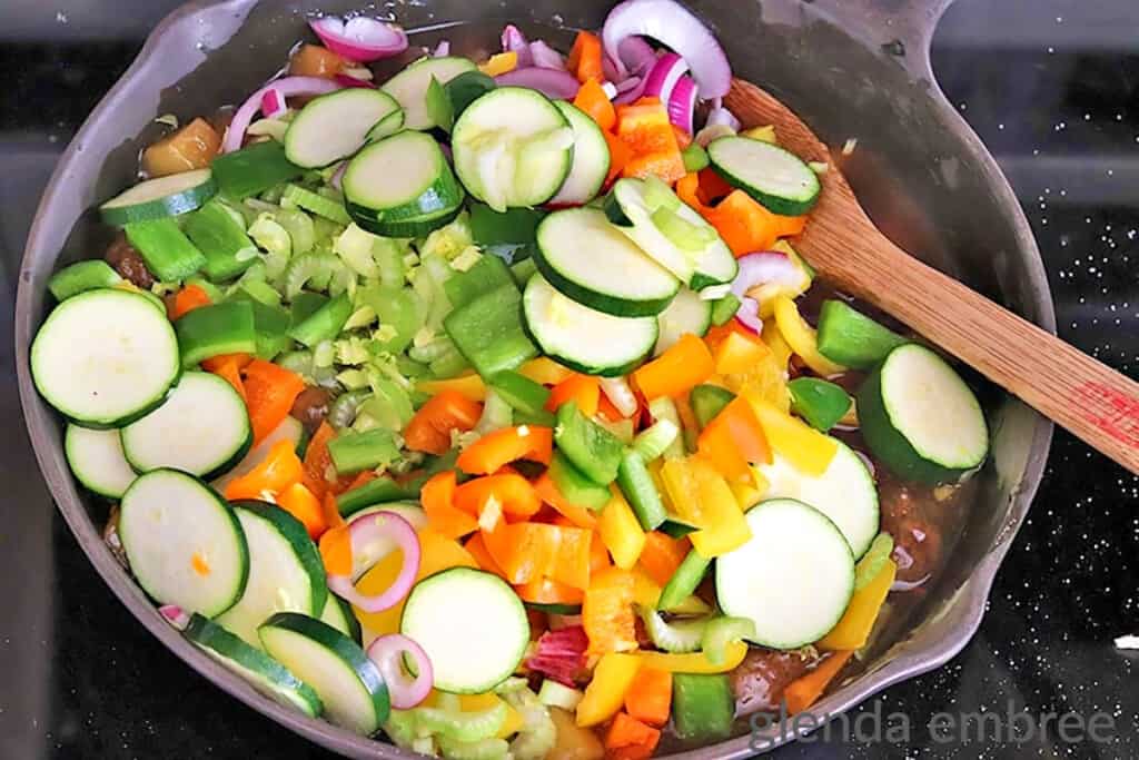 adding vegetables to Sweet and Sour Meatballs in a castiron skillet