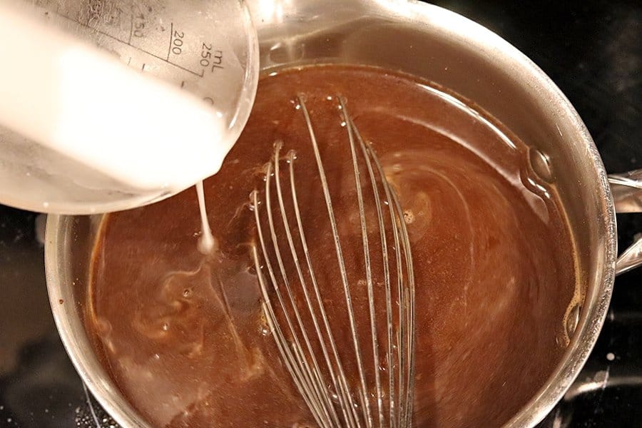 whisking corn starch slurry into beef broth in a sauce pan