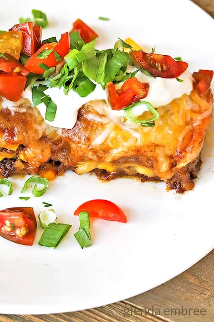 Beef Enchilada Casserole on a White plate sitting on a wooden table.