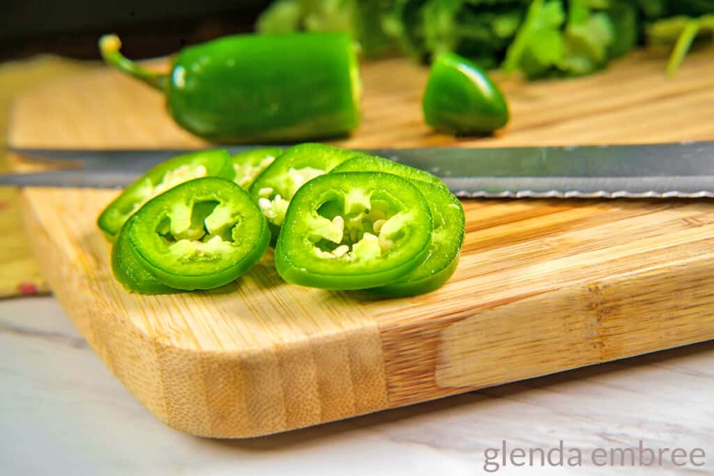 jalapenos being sliced on a wooden cutting board
