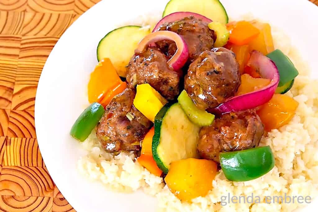 Sweet and Sour Meatballs on white rice served on a plain white plate sitting on a wooden table