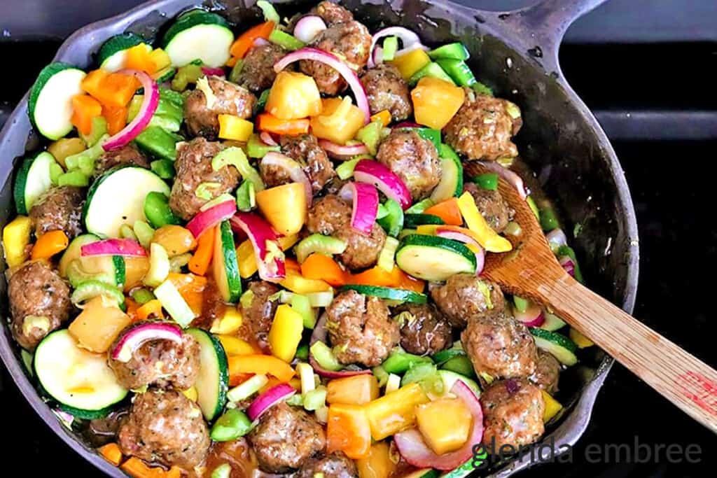 Sweet and Sour Meatballs in a Cast Iron skillet with a wooden spoon