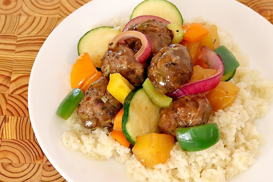 sweet and sour meatballs over white rice on a white plate that is sitting on a wooden table top