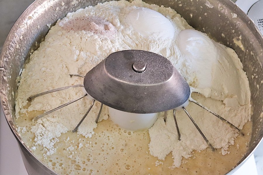 Adding the dry ingredients to the bowl of a stand mixer when making banana bread.