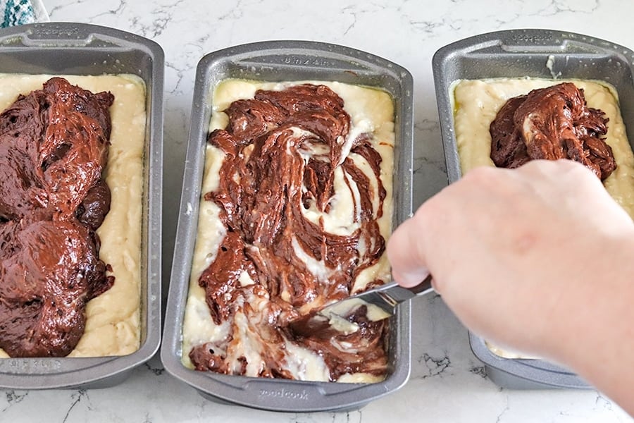 Using a butter knife to swirl chocolate batter into banana bread batter.