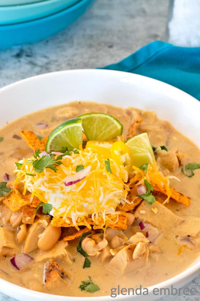 creamy white chicken chili in a white ceramic bowl on a concrete countertop with a turquoise cloth napkin to the right of the bowl