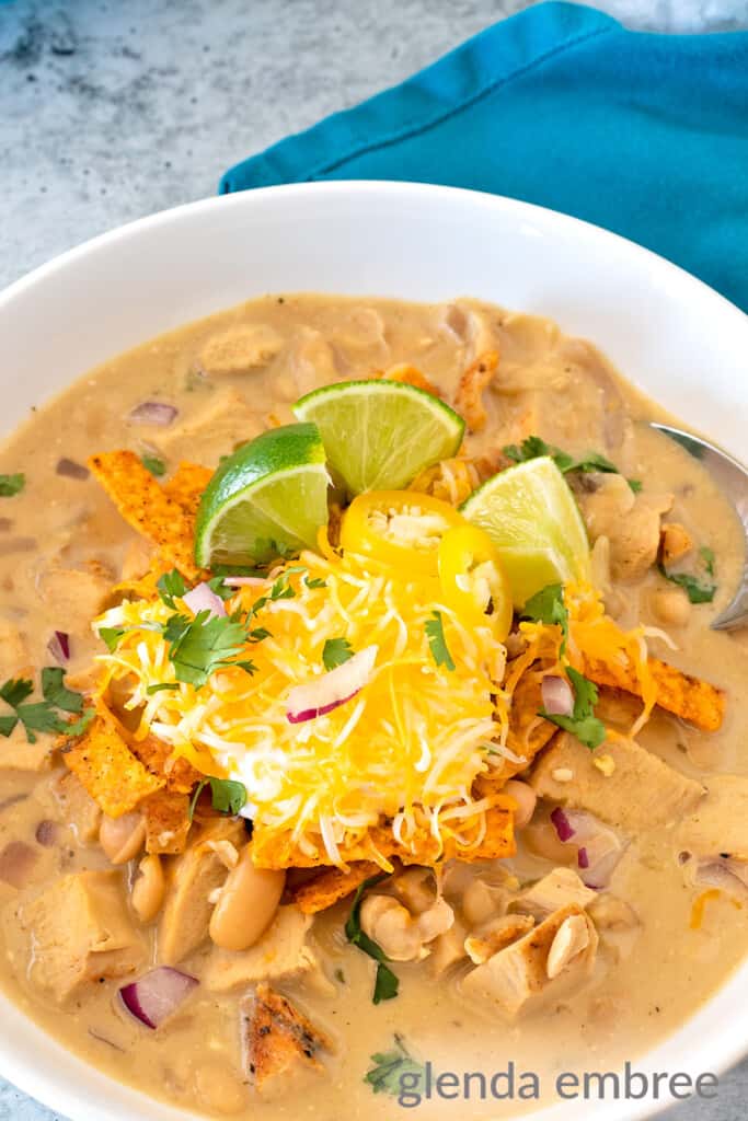 creamy white chicken chili in a white ceramic bowl on a concrete countertop with a turquoise cloth napkin to the right of the bowl