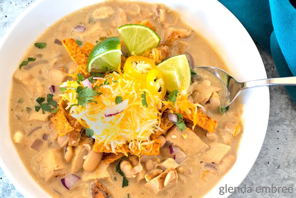 creamy white chicken chili in a white ceramic bowl on a concrete countertop with a turquoise cloth napkin to the right of the bowl