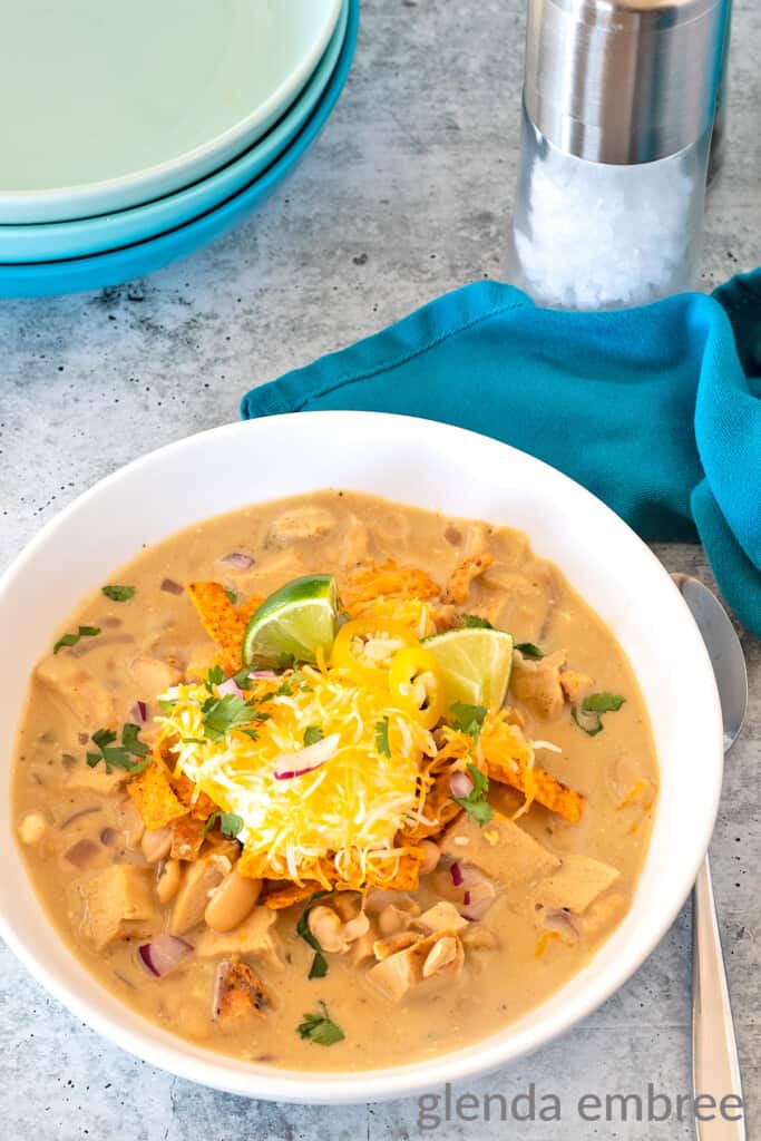 creamy white chicken chili in a white ceramic bowl on a concrete countertop with a turquoise cloth napkin to the right of the bowl