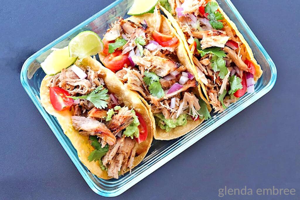 3 pork carnitas tacos in a clear rectangular dish on a blue counter