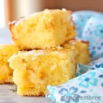 cut sweet cornbread squares stacked on a wooden board with a blue floral print fabric napkin