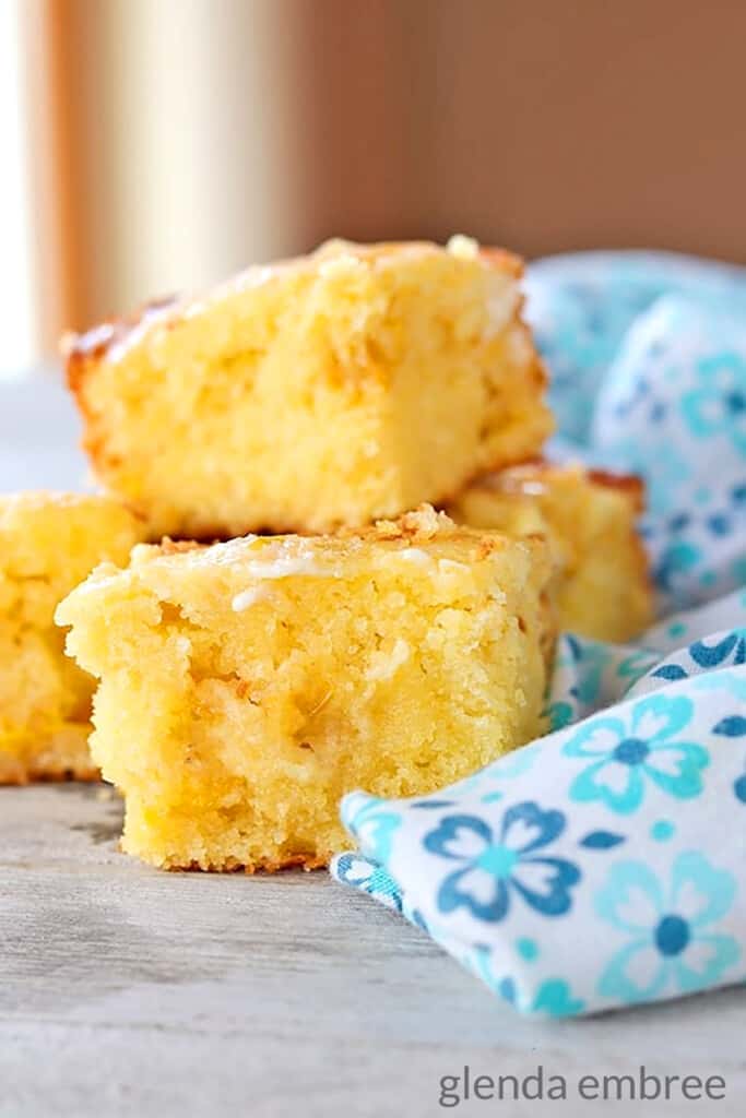 cut cornbread squares stacked on a wooden board with a blue floral print fabric napkin