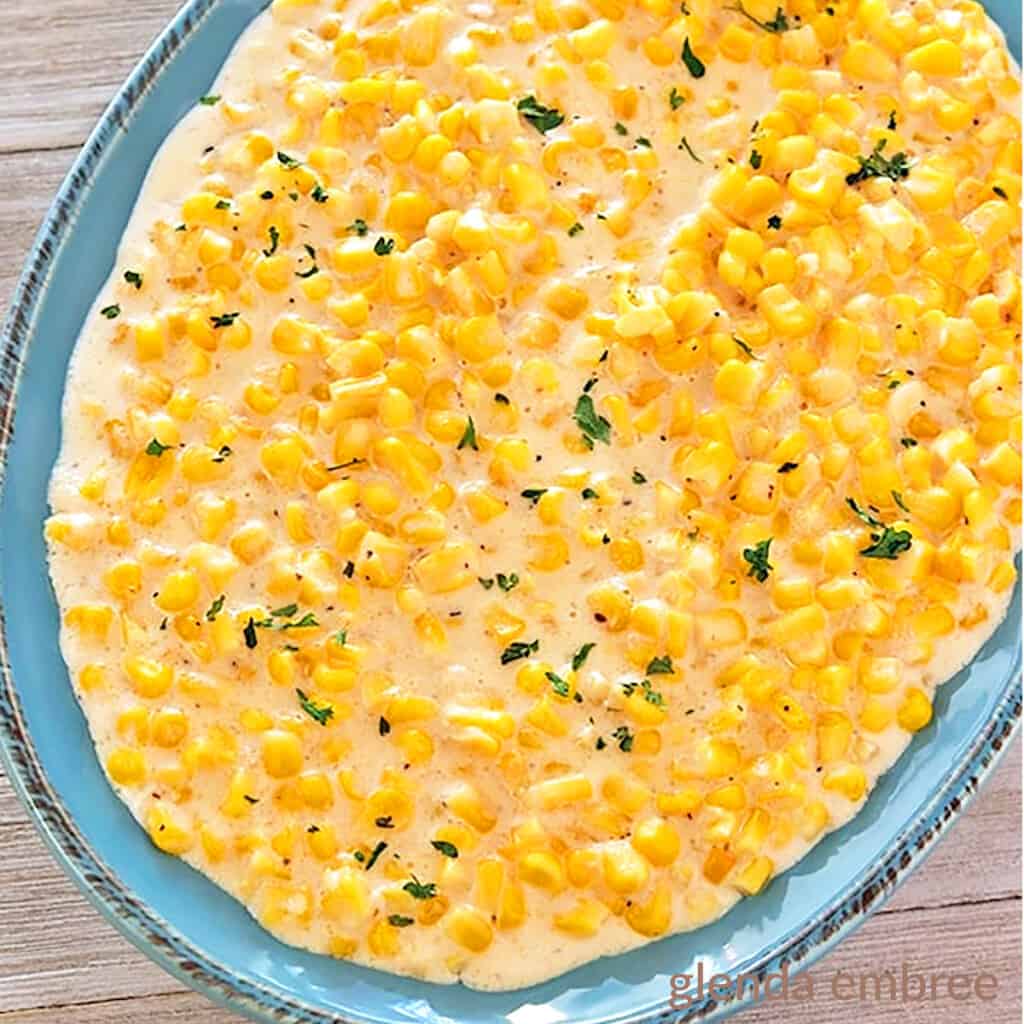 slow cooker creamed corn in a blue stoneware bowl on a barnboard table