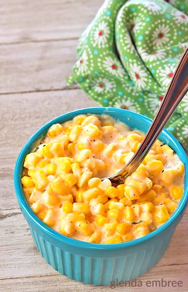 slow cooker creamed corn in a turquoise single-serve ramekin on a barnboard table wth a green and white print napkin