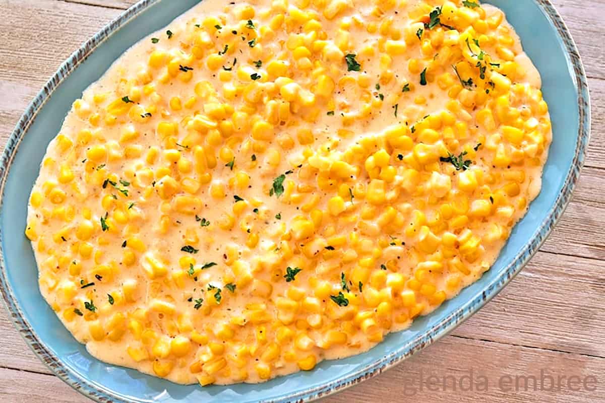 Slow cooker creamed corn in a blue stoneware bowl on a barnboard table.