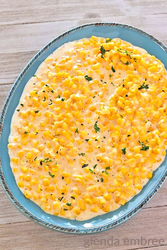 slow cooker creamed corn in a blue stoneware bowl on a barnboard table
