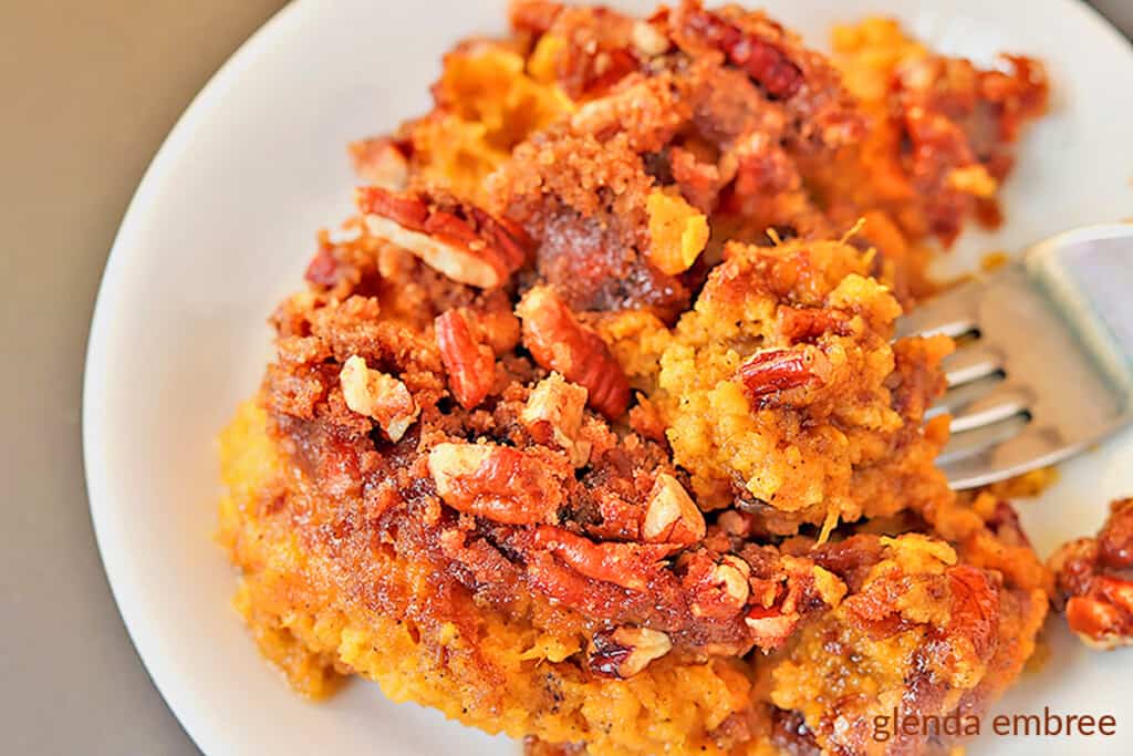 Sweet Potato Casserole on a white plate with a fork lifting a bite