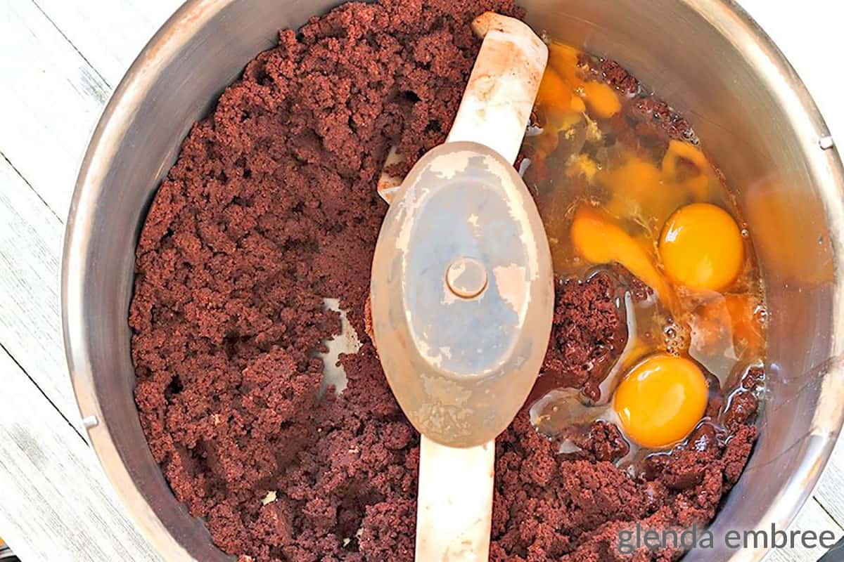 eggs being added to chocolate cookie dough in a stand mixer bowl