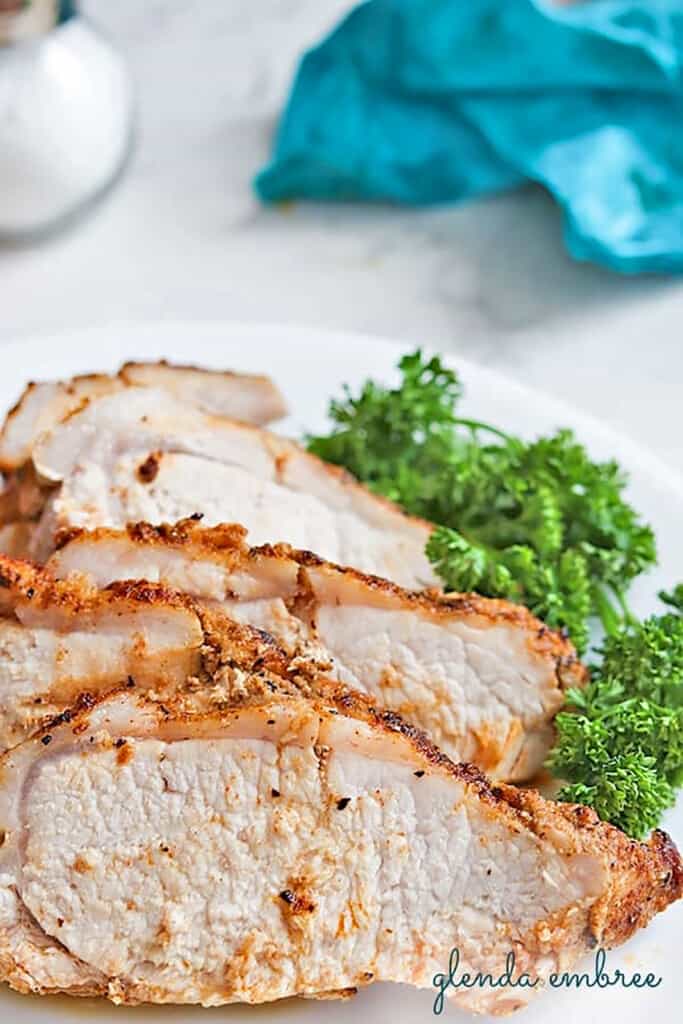 Thinly sliced Baked Pork Loin on a white plate with parsley garnish.