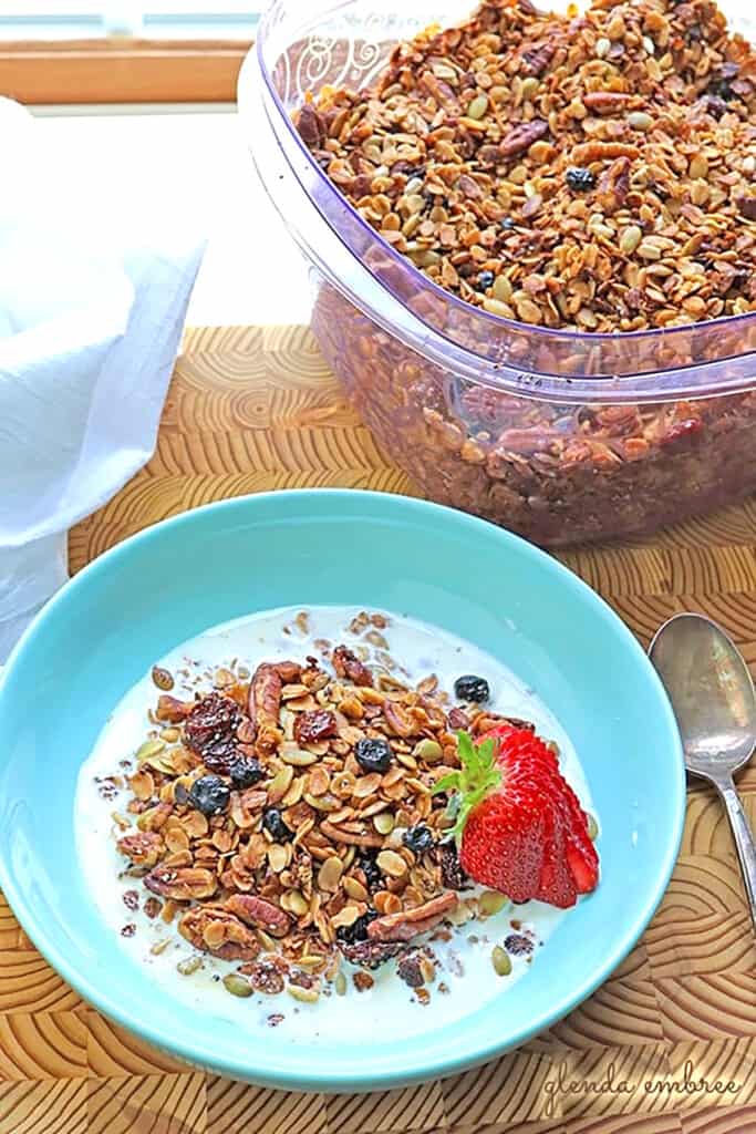 Gluten Free Granola in a turquoise bowl with milk. Container of granola sitting behind the bowl.