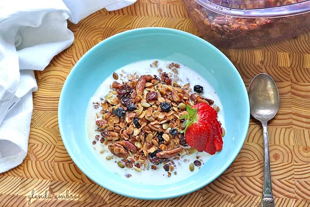 Gluten Free Granola in a turquoise bowl with milk. Container of granola sitting behind the bowl.