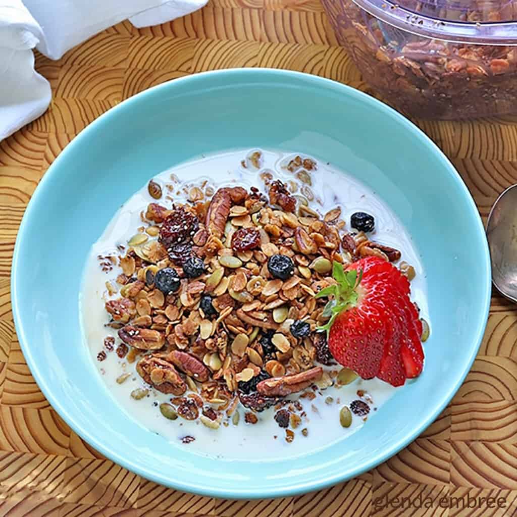 Quick and easy recipe for homemade gluten free granola in a blue stoneware bowl with fresh strawberry slices
