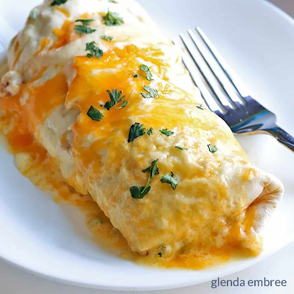 creamy chicken enchilada on a white plate with a fork