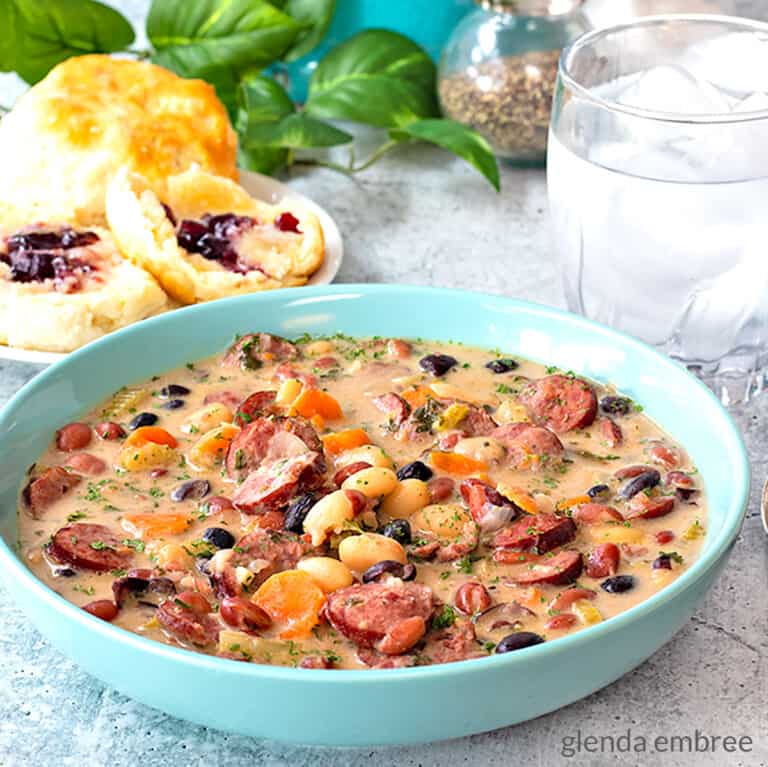bean soup in a blue stoneware bowl next to biscuits with butter and grape jelly