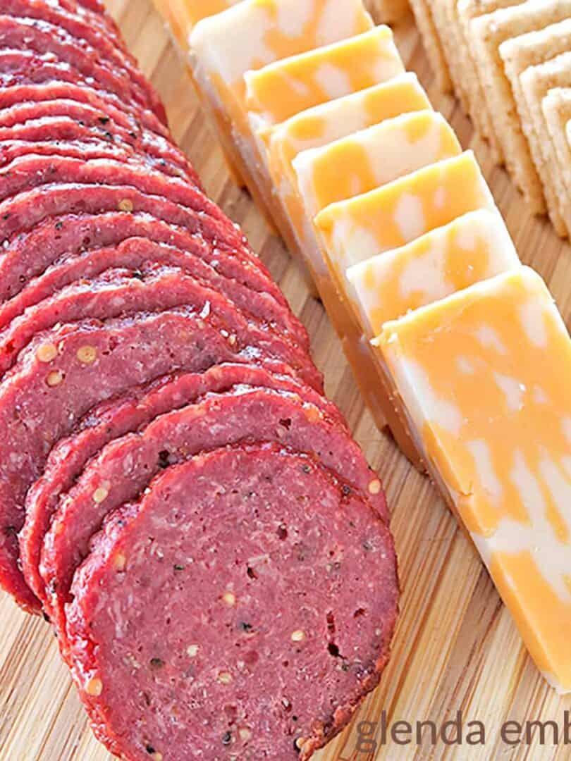 homemade beef summer sausage with cheese and crackers on a wooden cutting board