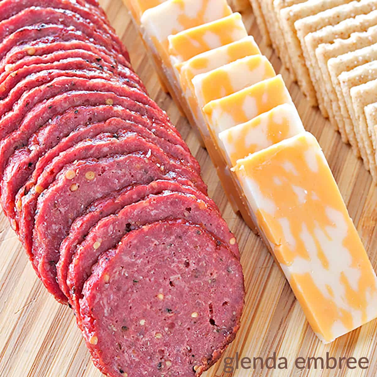 homemade beef summer sausage with cheese and crackers on a wooden cutting board