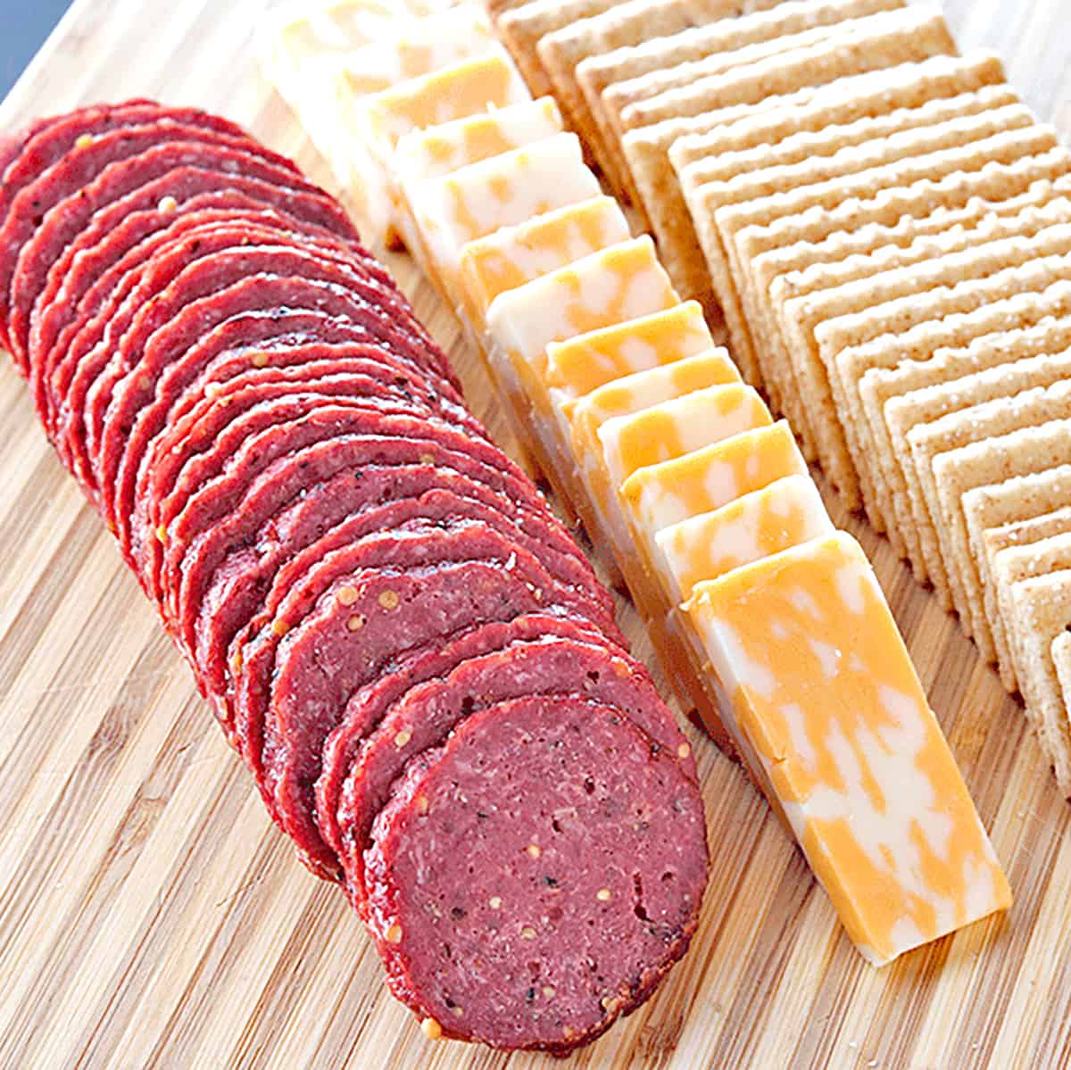 homemade beef summer sausage with cheese and crackers on a wooden cutting board
