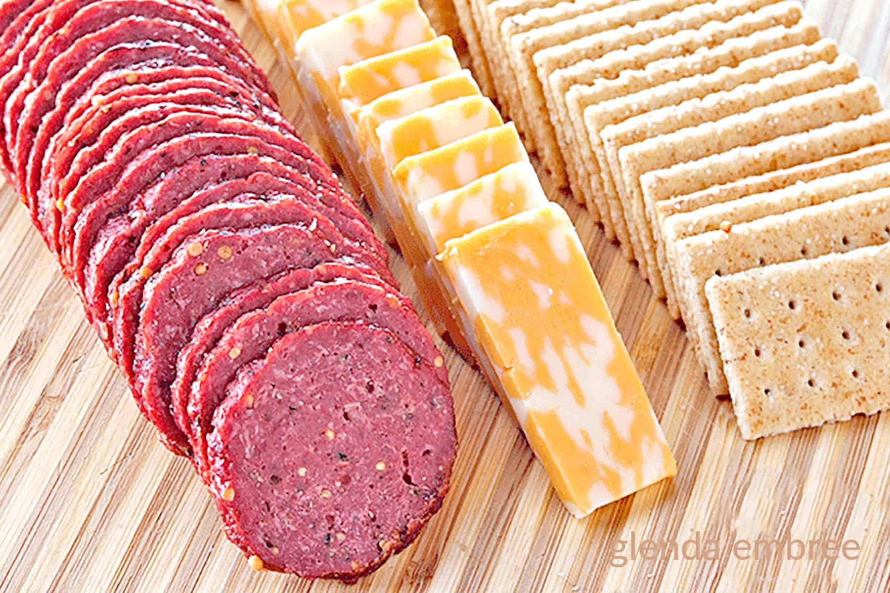 homemade beef summer sausage sliced on a wooden cutting board with cheese and crackers