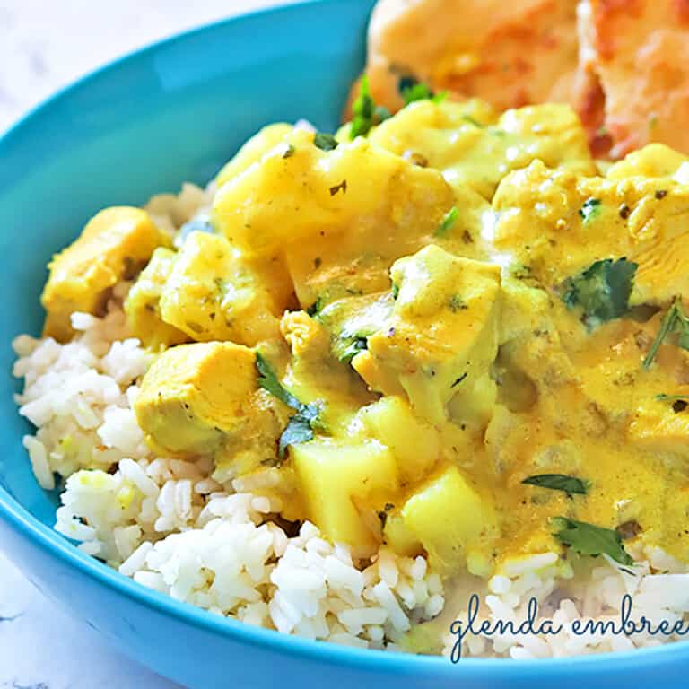 yellow Curry Chicken with potatoes served over rice with naan in a blue ceramic bowl on a marble countertop