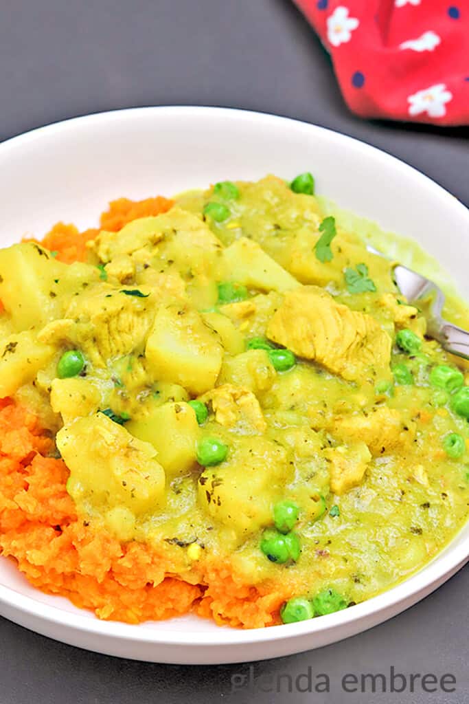 Yellow Chicken Curry with Potatoes and Peas over mashed sweet potatoes in a white bowl on a black table