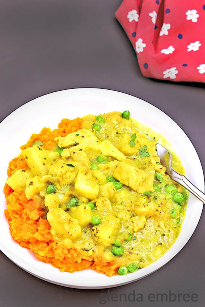 Yellow Chicken Curry with Potatoes and Peas over mashed sweet potatoes in a white bowl on a black table