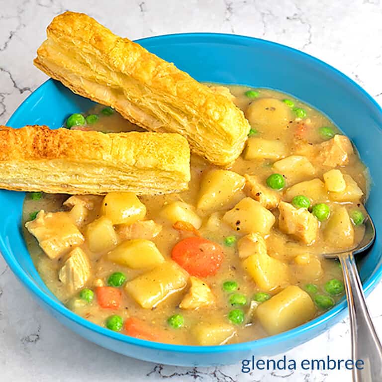 Chicken Pot Pie Soup in a blue stoneware bowl with two puff pastry sticks.