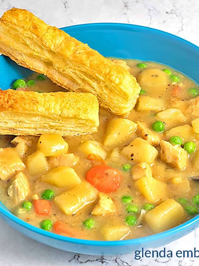 Chicken Pot Pie Soup in a blue stoneware bowl with two puff pastry sticks.