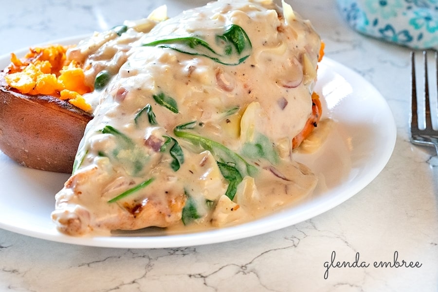 Creamy Spinach Artichoke Chicken on a plate with baked sweet potato.