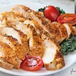 perfect baked chicken breasts sliced and served on a white plate with kale and grape tomatoes