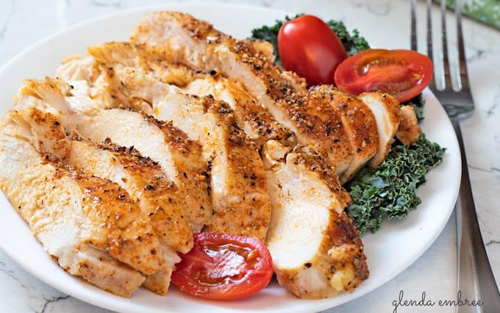 perfect baked chicken breasts sliced and served on a white plate with kale and grape tomatoes