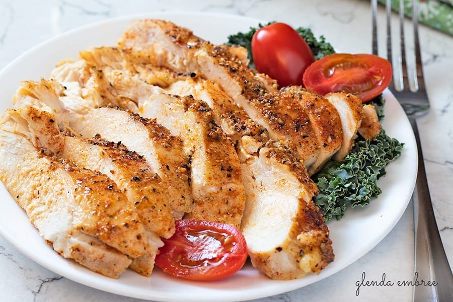 perfect baked chicken breasts sliced and served on a white plate with kale and grape tomatoes