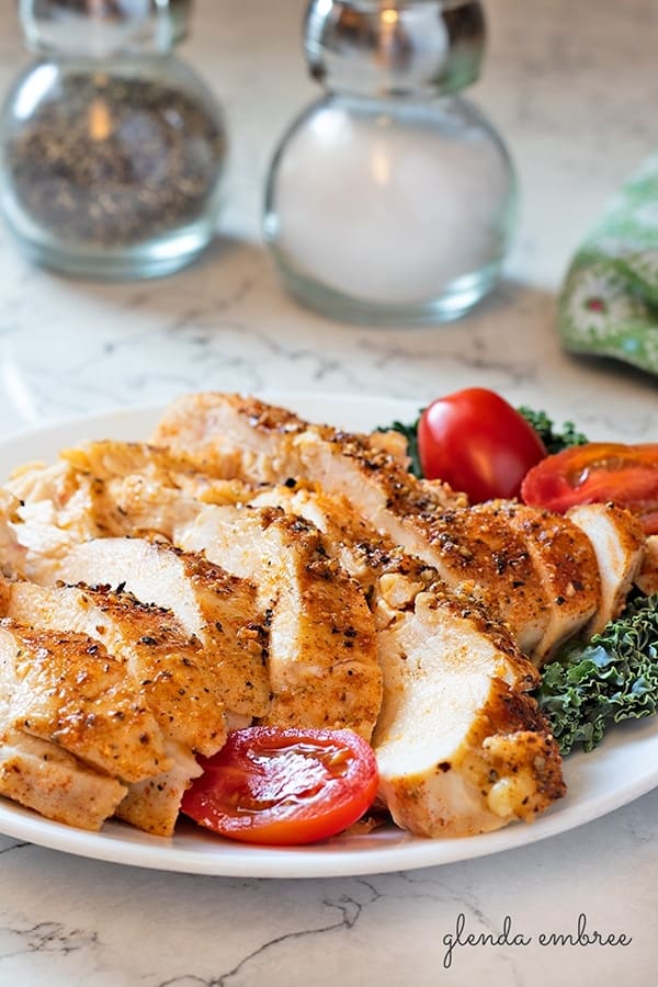 perfect baked chicken breasts sliced and served on a white plate with kale and grape tomatoes