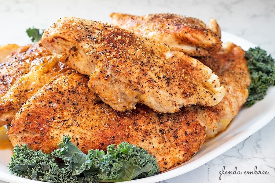 7 Perfect Baked Chicken Breasts, whole on a white serving platter with kale