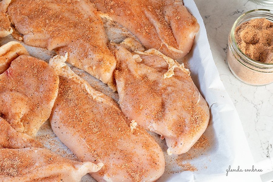 chicken breasts seasoned with all purpose seasoning on a parchment lined baking sheet