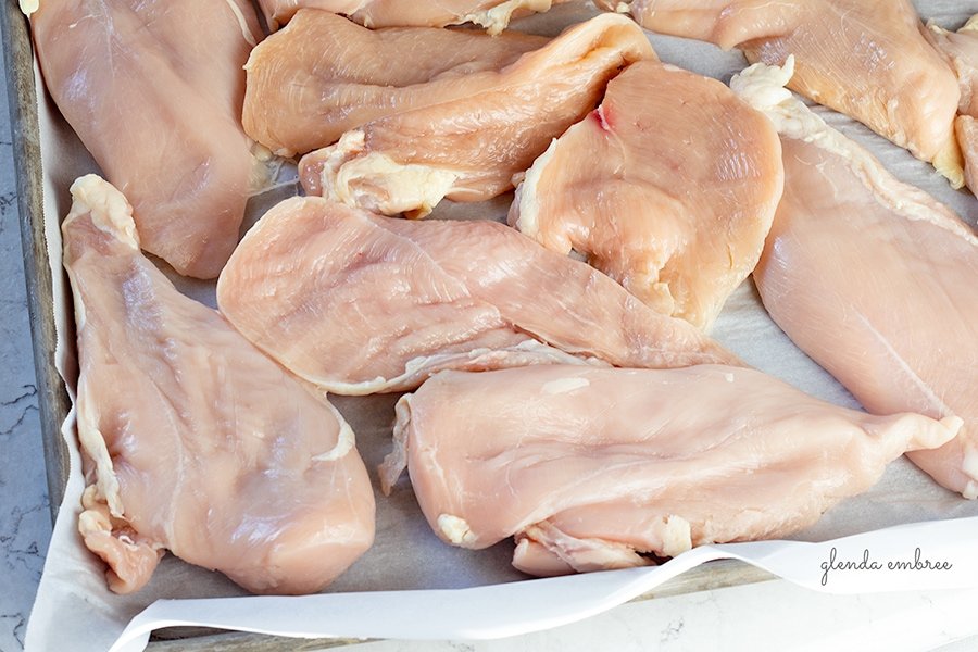 Boneless Skinless Chicken Breasts sliced and arranged on a rimmed baking sheet lined with parchment paper