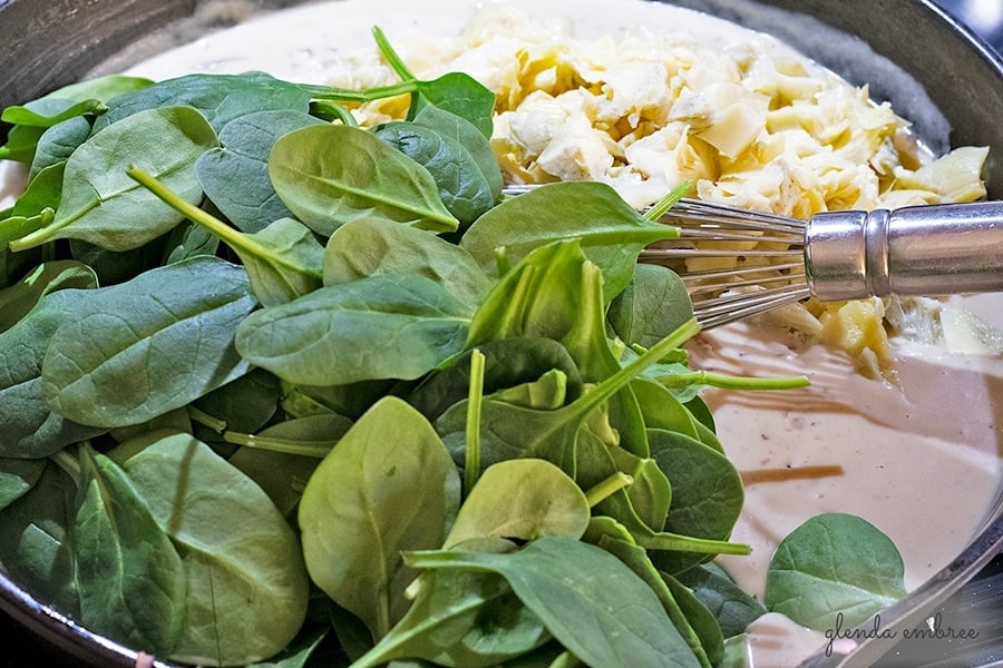 adding baby spinach and artichoke hearts to the sauce for Creamy Spinach Artichoke Chicken